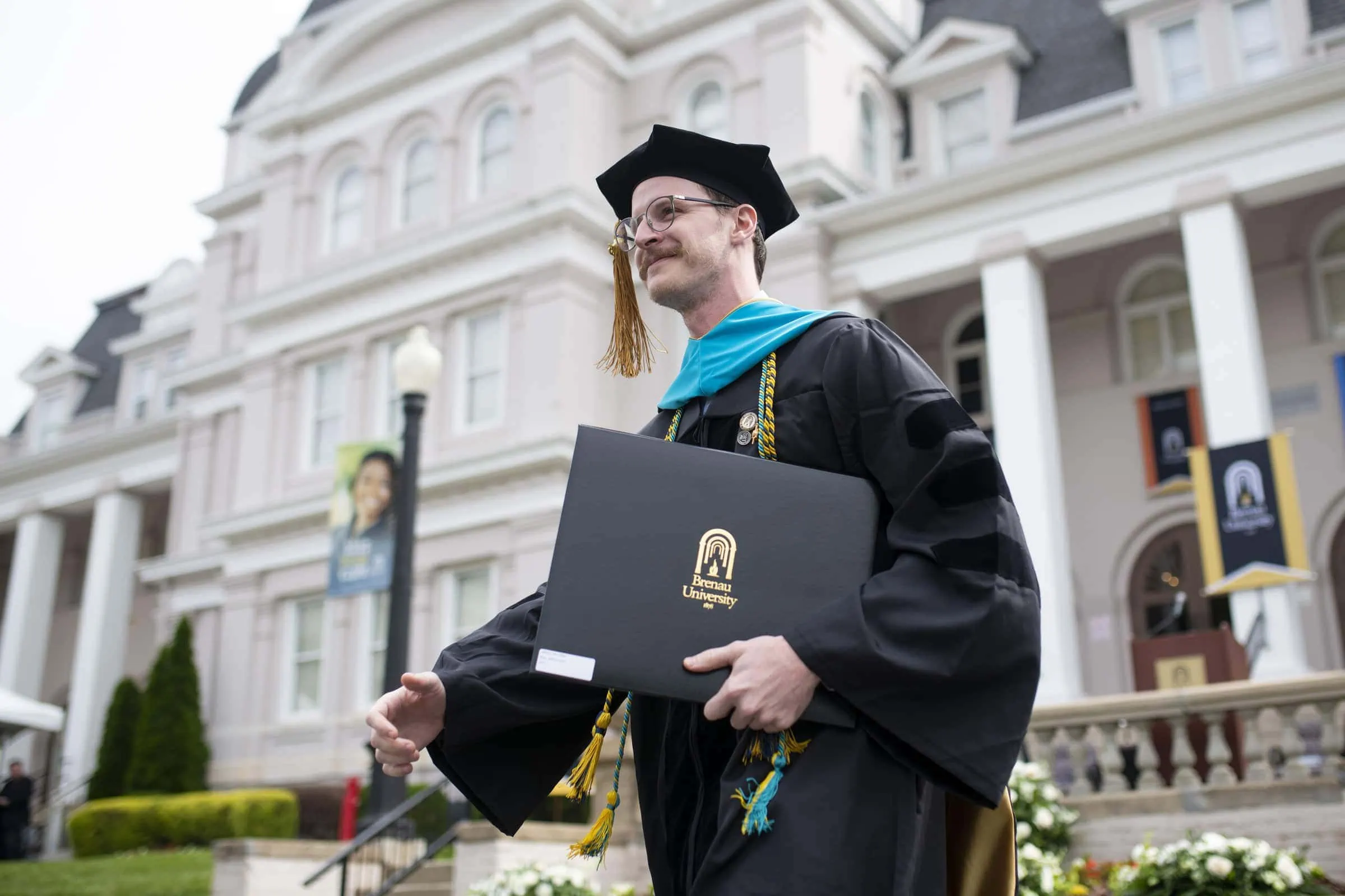 Graduate in cap and gown holding diploma at Brenau University commencement ceremony.